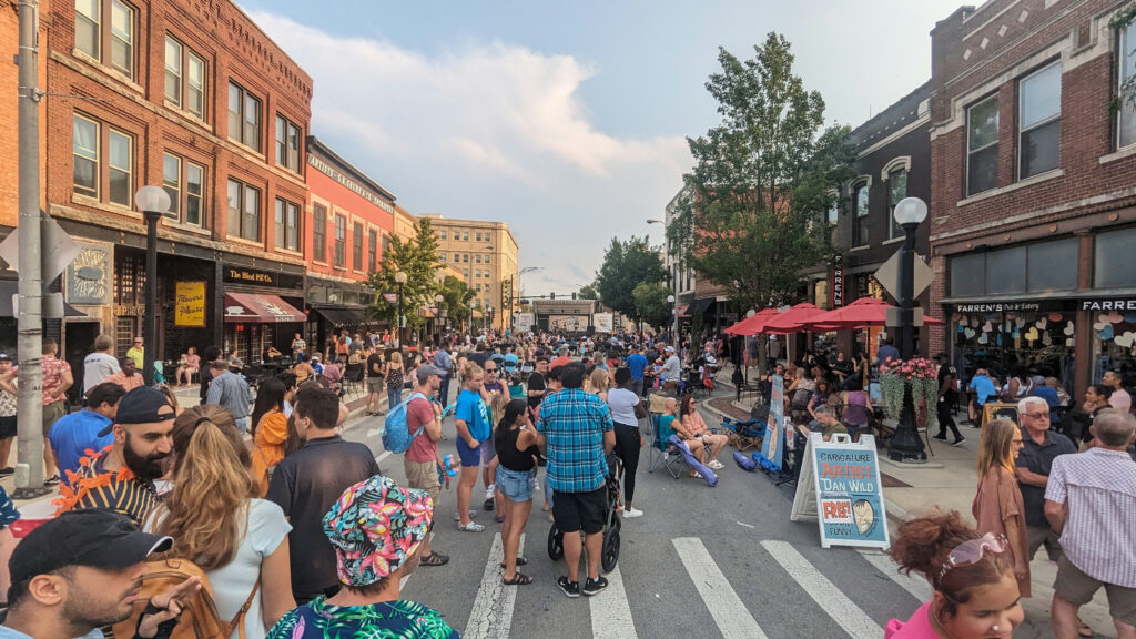 Large group of people outside on a pedestrian only street, enjoying music and food.