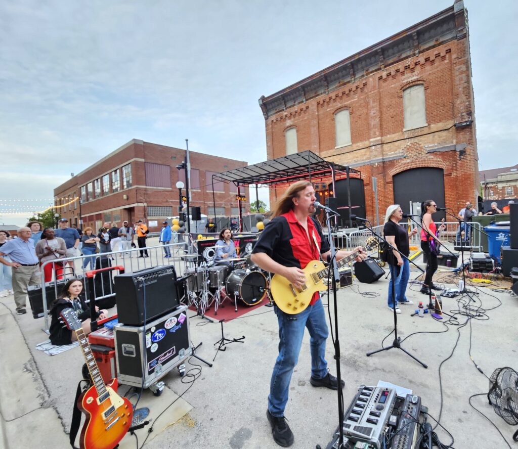 Wide angle image of a band performing on Market Street. The focus is on the guitarist who is singing.